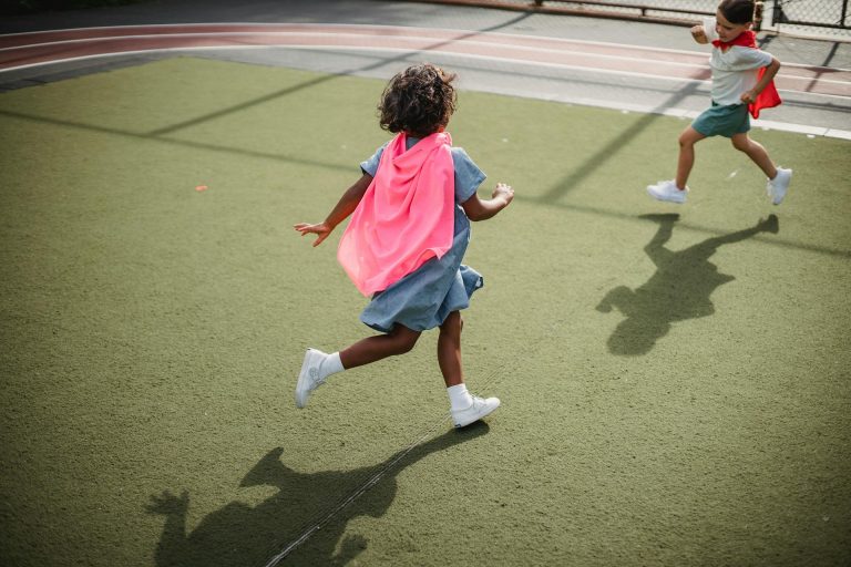 Two children playing a running game wearing capes.